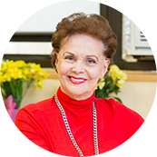 Portrait of Joanna wearing red turtle neck and yellow flowers in the background.