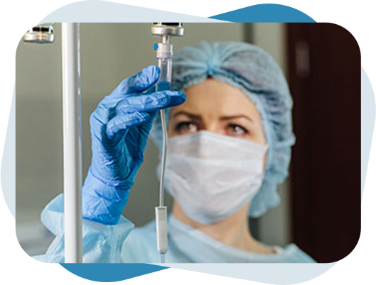 Nurse wearing personal preventive equipment and checking IV set chamber before introducing medicine to the patient as part of IV therapy.