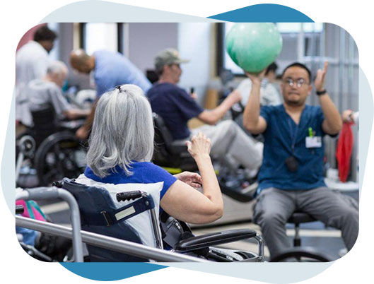 Neurological Diseases Care Woman sitting on wheelchair playing pass the ball with physical therapist.