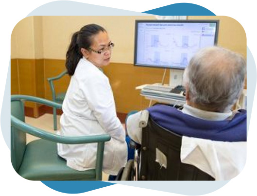 Nurse looking at speech therapy charts on a computer screen while guiding an elderly man.