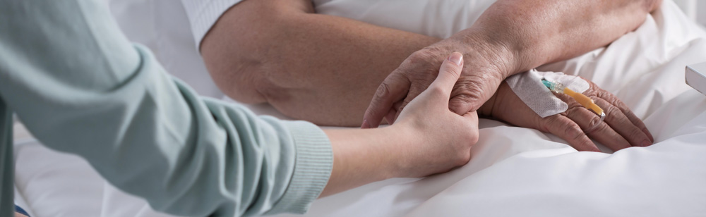 Nurse holding patients hand and providing palliative care at Fairview Rehab & Nursing Home