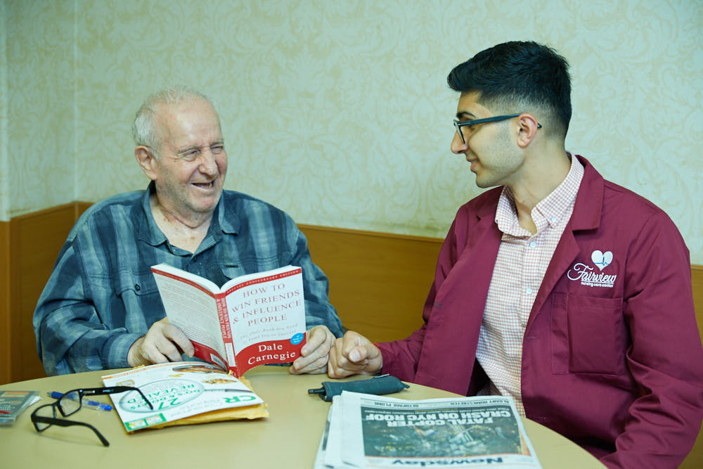 An elderly patient smiling while reading the book as a part of recreation therapy to prevent memory loss