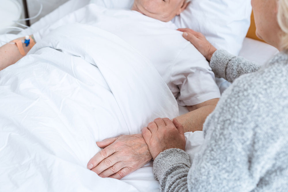 Senior woman holding elderly man's hand suffering from bedsores