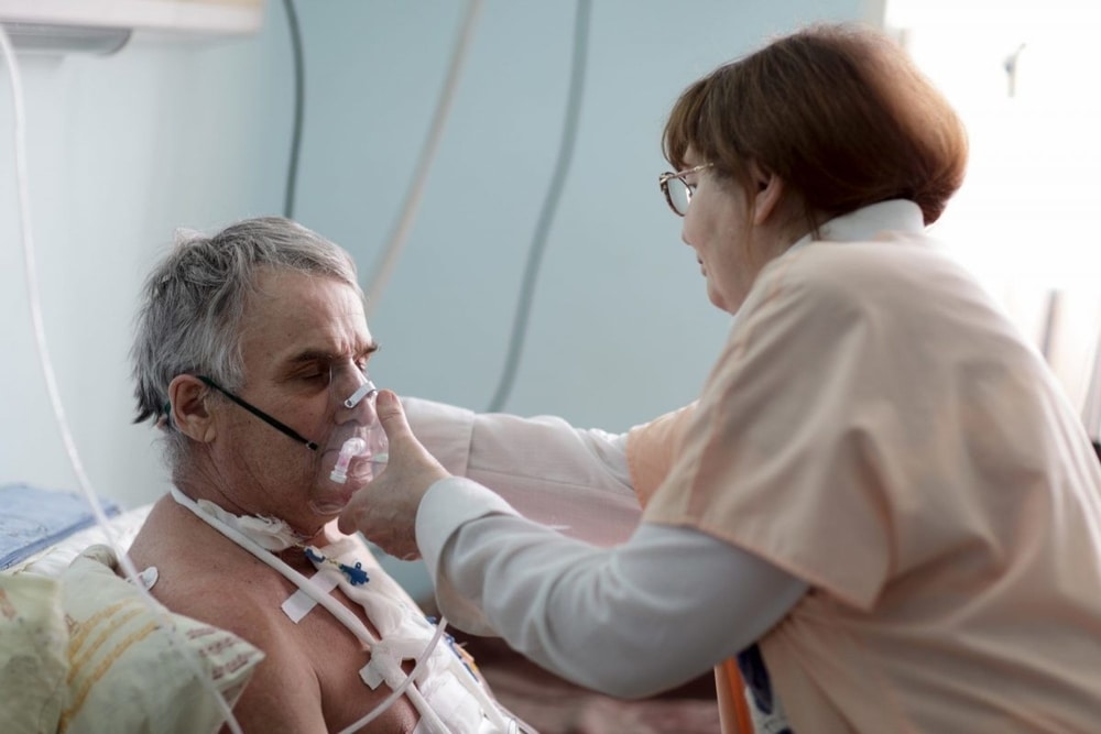 Nurse providing respiratory therapy to a senior man lying on the bed.