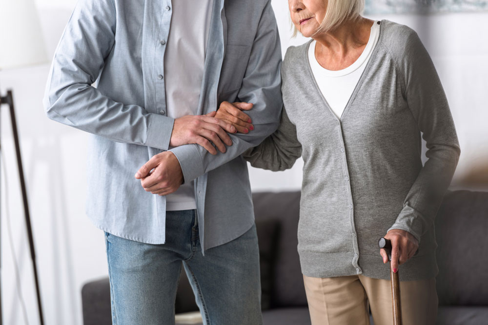 A person helping a senior woman with walking problems