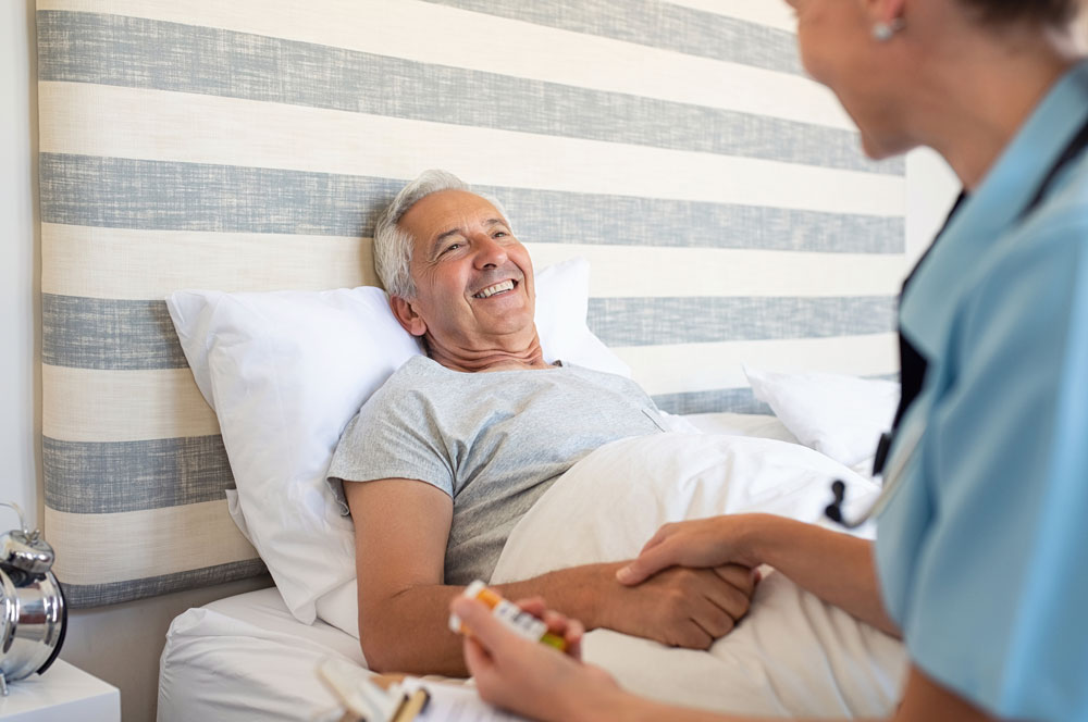 Nurse holding elderly man hands lying on the bed due to prolonged fatigue and providing after surgery care