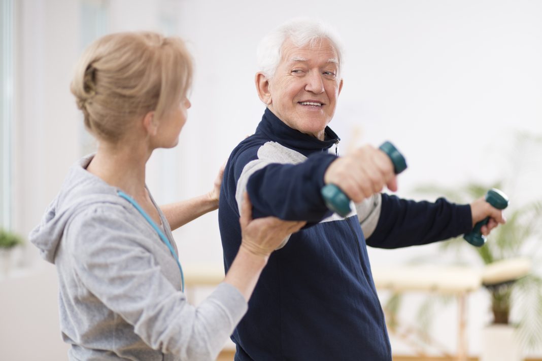 Therapist helping elderly man with exercise during short-term rehab program