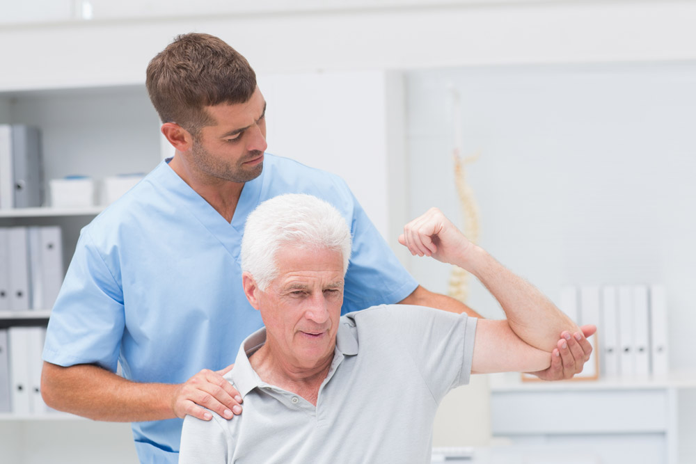 Physiotherapist giving physical therapy to elderly man suffering from shoulder pain