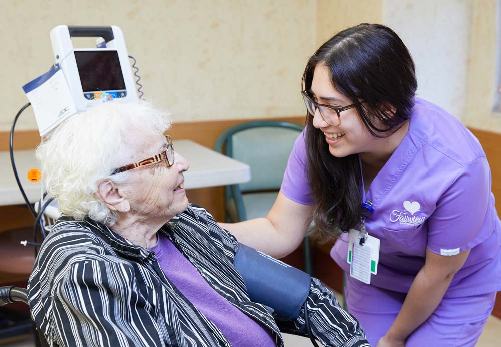 Nurse checking blood pressure of an elderly woman with broken hand and providing occupational therapy.