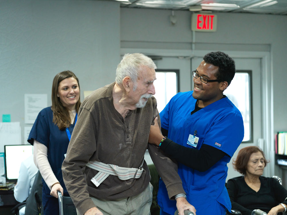Nursing staff helping elderly man with physical therapy to improve range of motion.