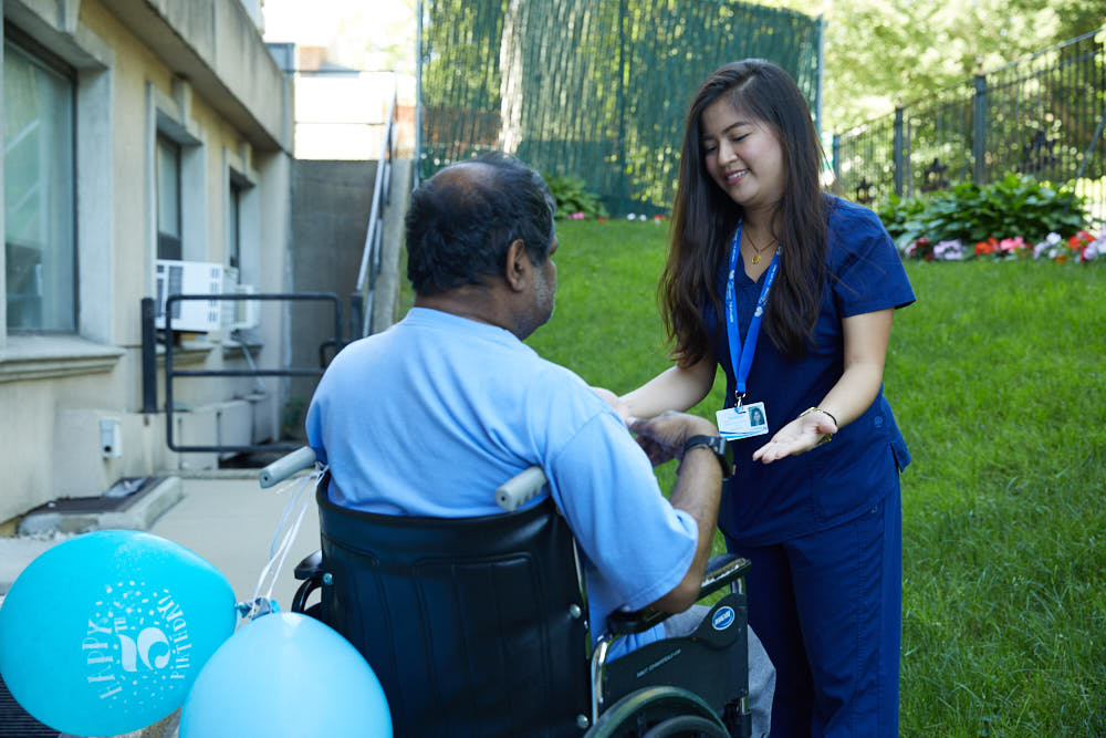 Nurse providing post operative care to a patient sitting on a wheel chair to recover after spinal fusion