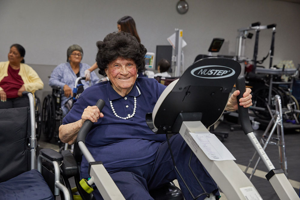 Elderly woman with arthritis symptoms doing exercise on a machine to prevent arthritis from worsening.