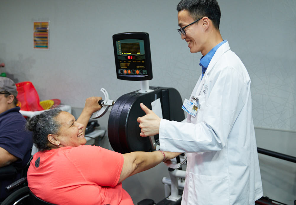 Physical therapist helping elderly woman suffering from impaired vascular circulation in getting physical therapy on a machine.