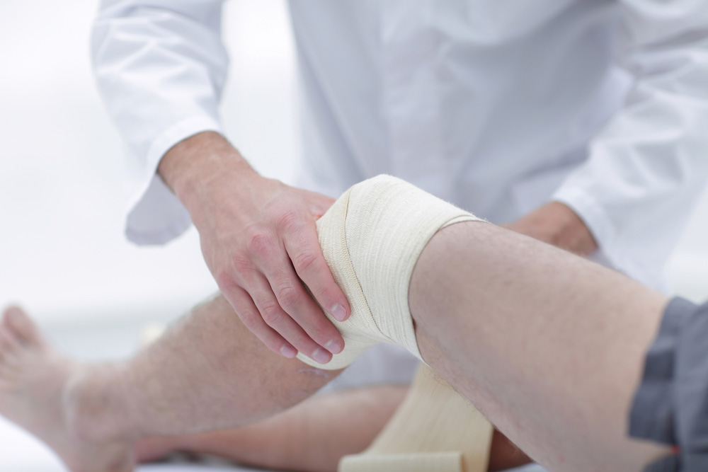 Doctor providing treatment to a patients wound on his leg.