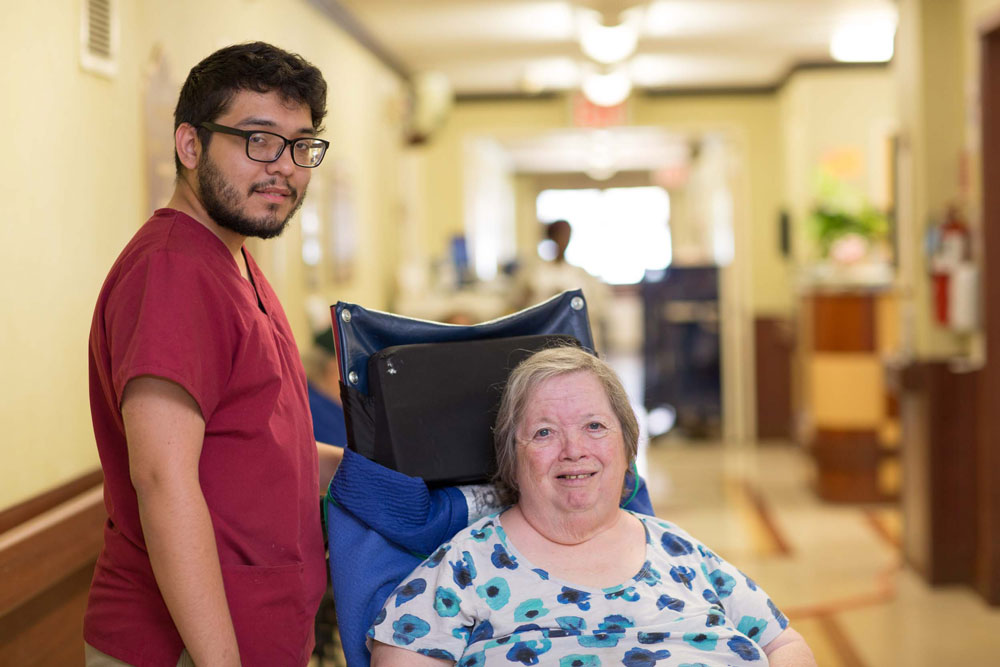 Male nursing staff providing care to elderly woman sitting on a wheelchair suffering from severe arthritis