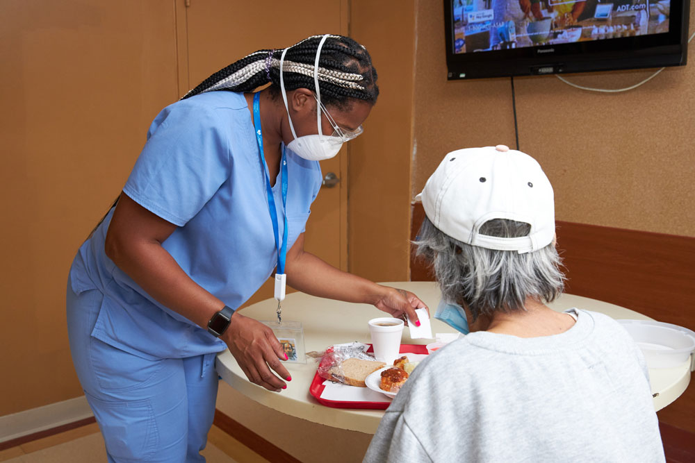 Black nurse providing aide to a senior woman with trouble swallowing.