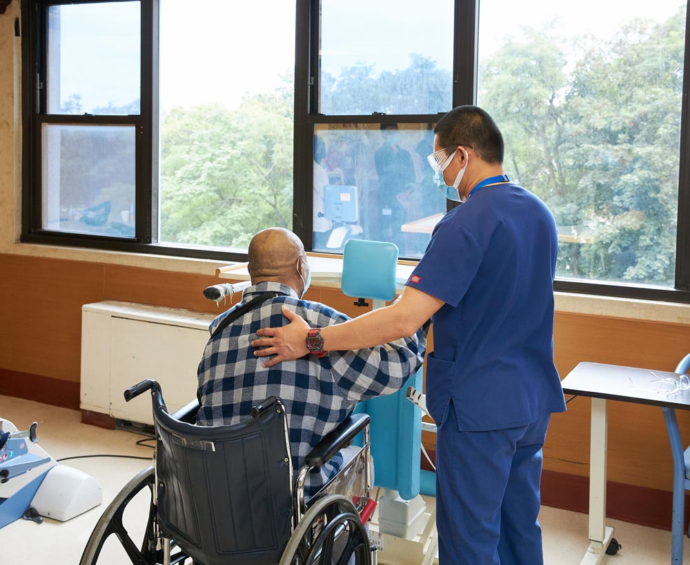 Physical therapist helping senior man with rehab and exercise suffering from spinal injury