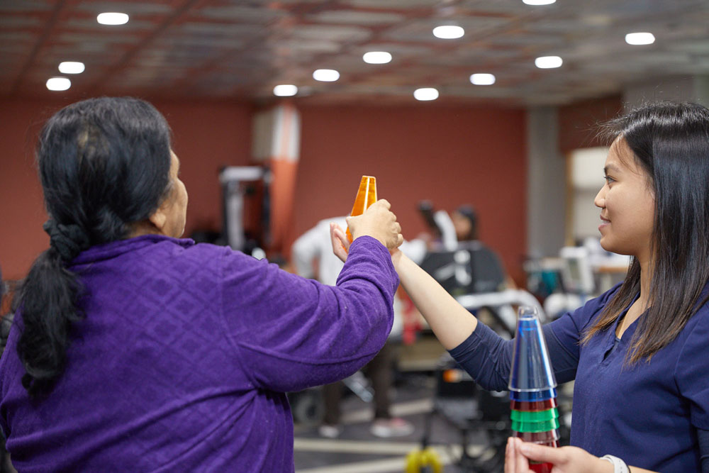 Nurse providing outpatient rehab services to a senior woman with brain injury and playing games with cups