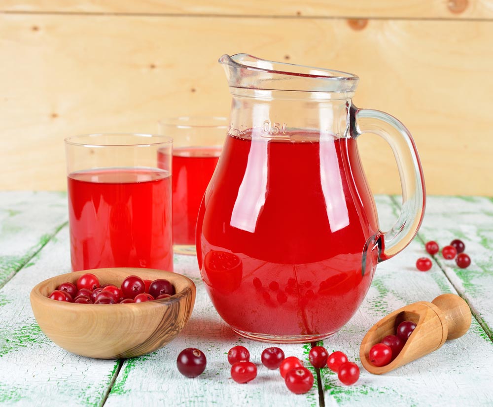 Cranberry juice in jug and glasses with some Cranberries in the bowl which are good foods for the liver.