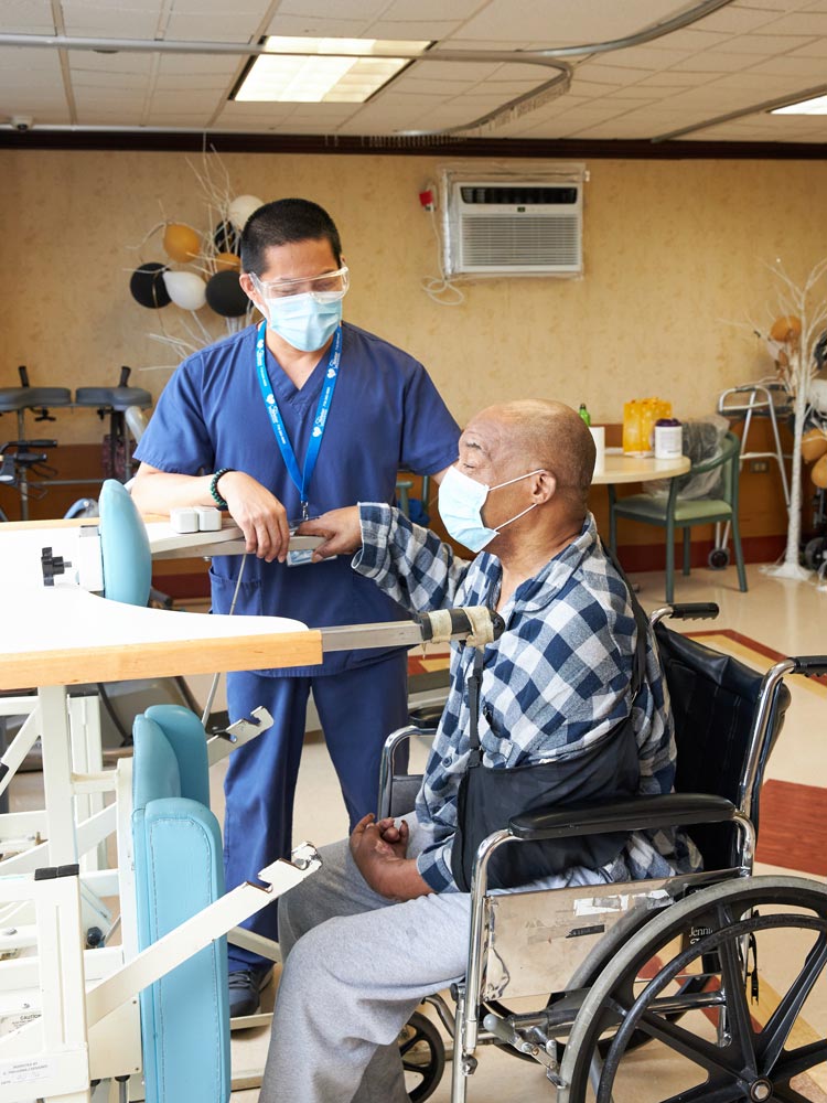 Physical therapist helping senior man sitting on a wheel chair in physical therapy to improve heart health.