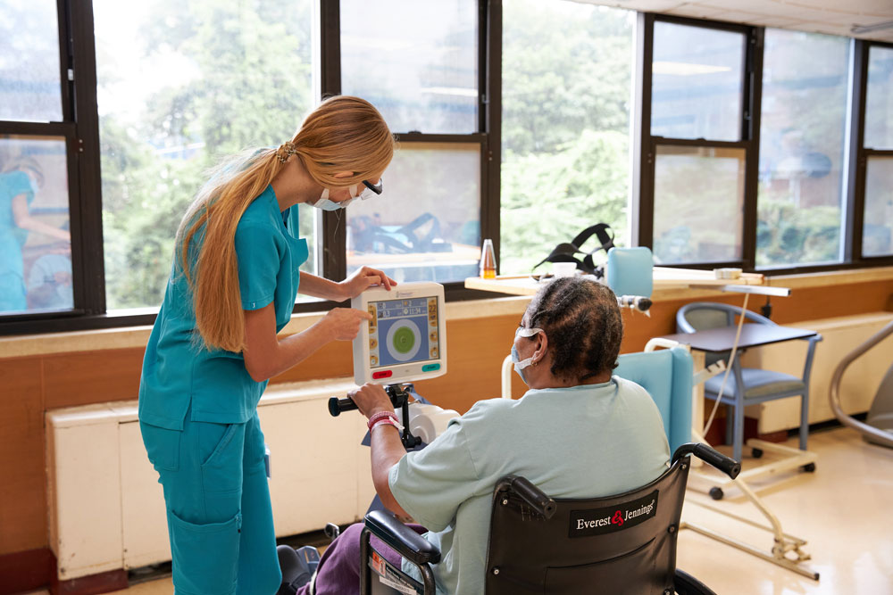Physical therapist guiding senior woman sitting on a wheelchair going through rehab after orthopedic surgery.