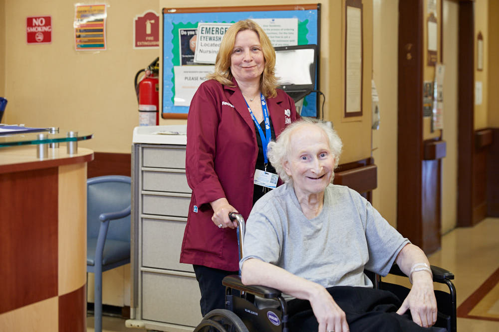 Female nurse and a senior woman on a wheelchair suffering from multiple sclerosis symptoms.