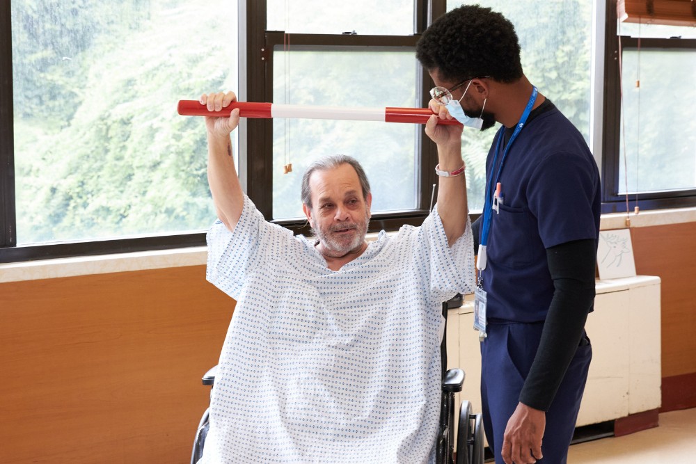 Therapist helping senior man sitting on a wheel chair with exercise in order to stay healthy to prevent the dangers of heart disease.