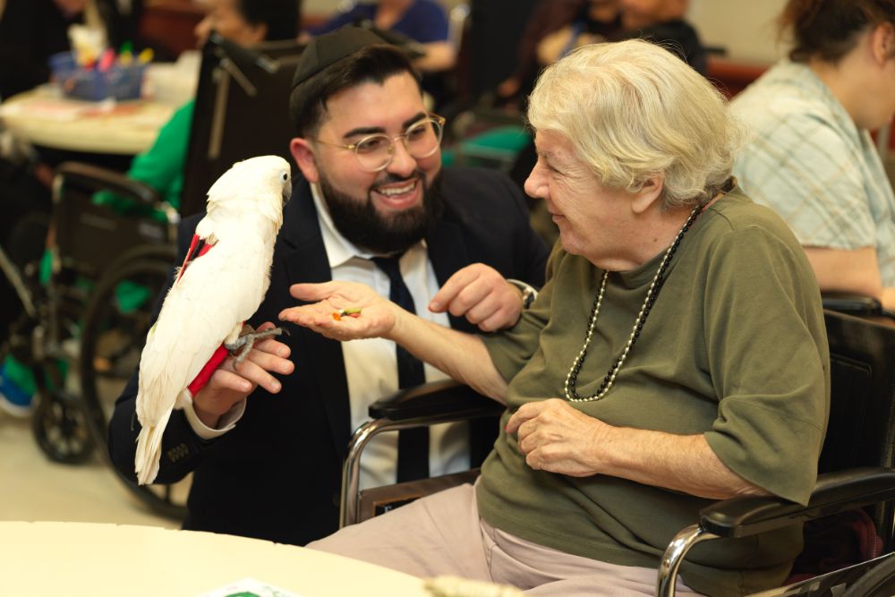 Therapist with an elderly woman and parrot during pet therapy session to keep them happy despite illness.