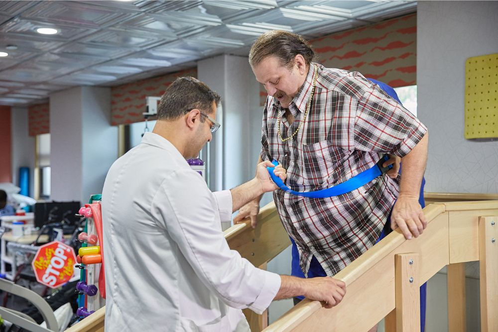 Therapist helping man with balancing physical therapy for post-accident therapy.