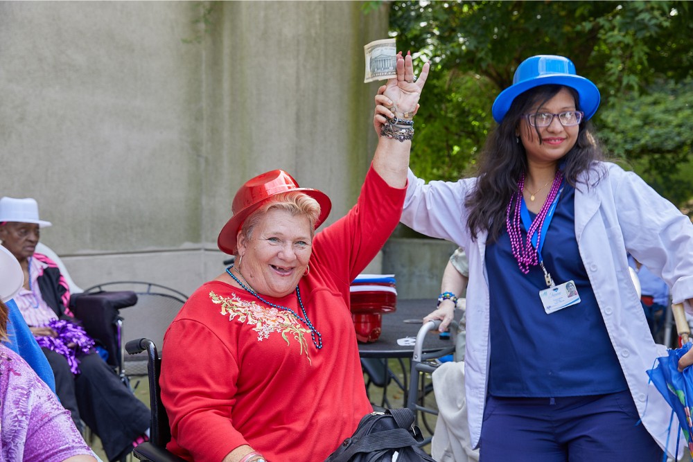 Brain Healthy Lifestyle Nurse supporting a smiling older woman during an outdoor celebration, promoting social engagement as part of a brain healthy lifestyle.