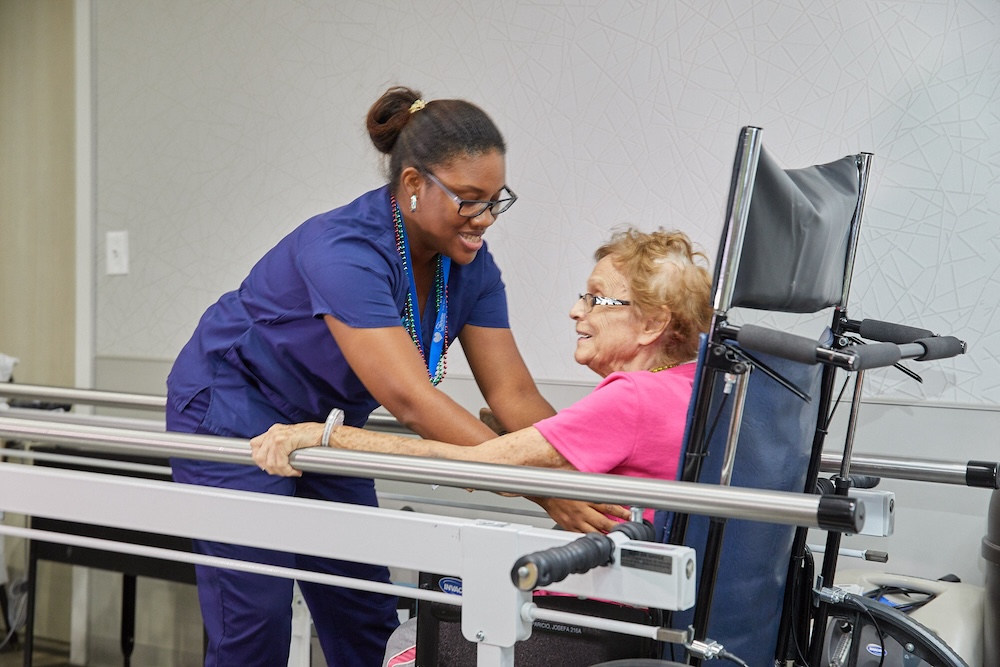 Therapist assisting an elderly woman with walking exercises using parallel bars, focusing on improving physical strength neurological function through rehabilitation therapy.