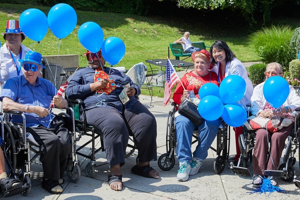 Group of seniors enjoying an outdoor summer celebration with balloons and flags, highlighting the benefits of outdoors in summer through fresh air, social interaction, and recreation.