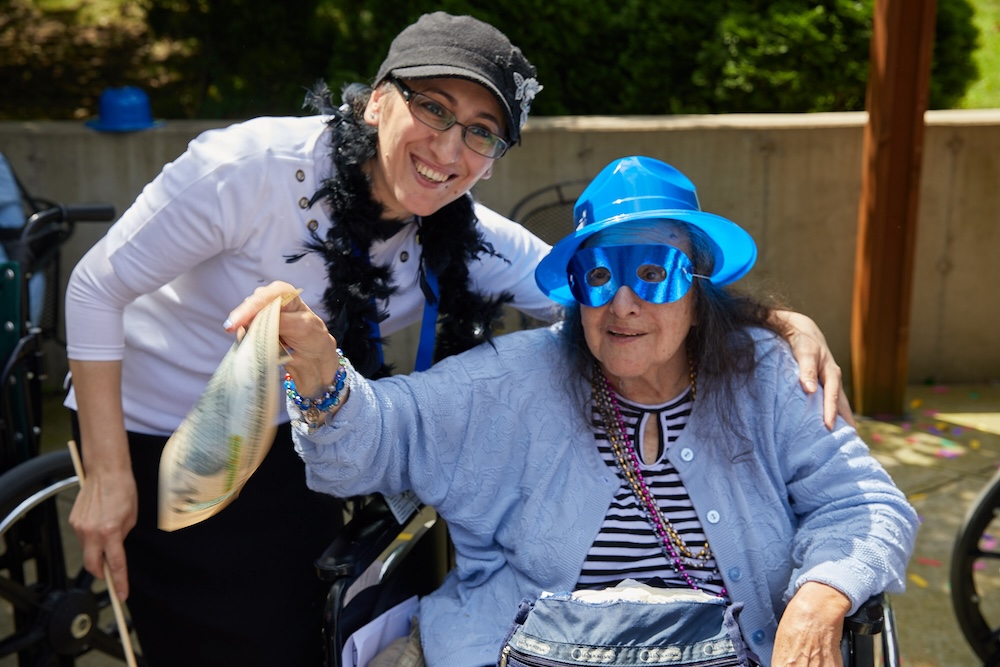 Smiling elderly woman with dementia enjoying an outdoor social activity with a caregiver, highlighting the positive impact of companionship and engagement.