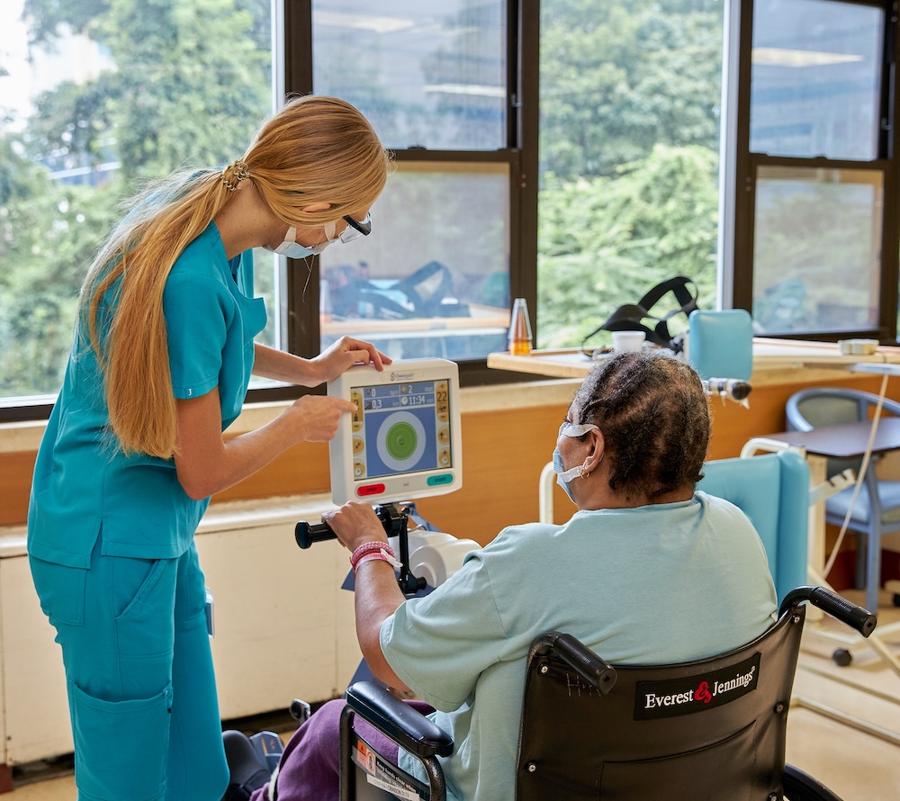 TBI recovery fitness Physical therapist guiding a patient in a wheelchair through rehabilitation exercises using fitness equipment, supporting tbi recovery fitness and improved mobility after a traumatic brain injury.